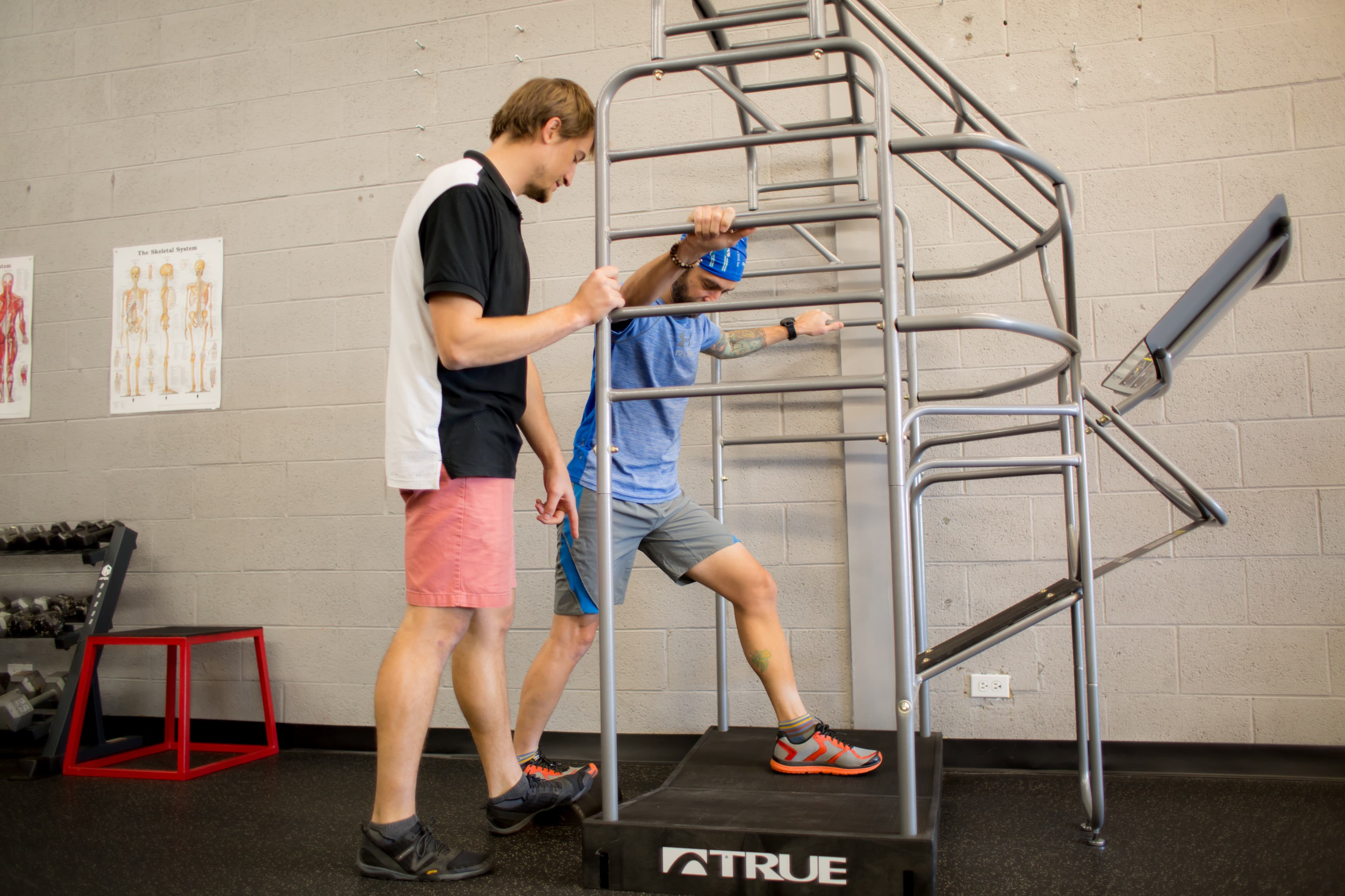 A therapist coaches a patient working out on a stepper machine in the clinic